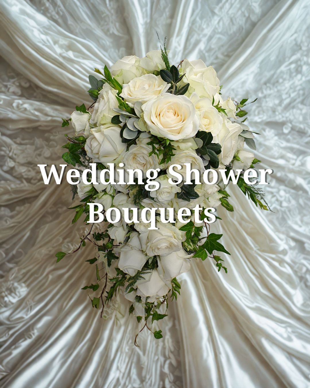 Bouquet of white roses and green leaves against silky white fabric background